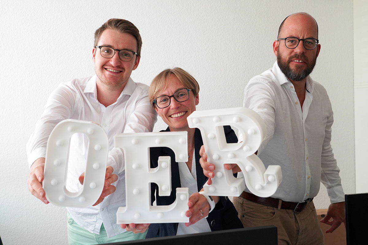Drei Personen halten die OER Buchstaben hoch