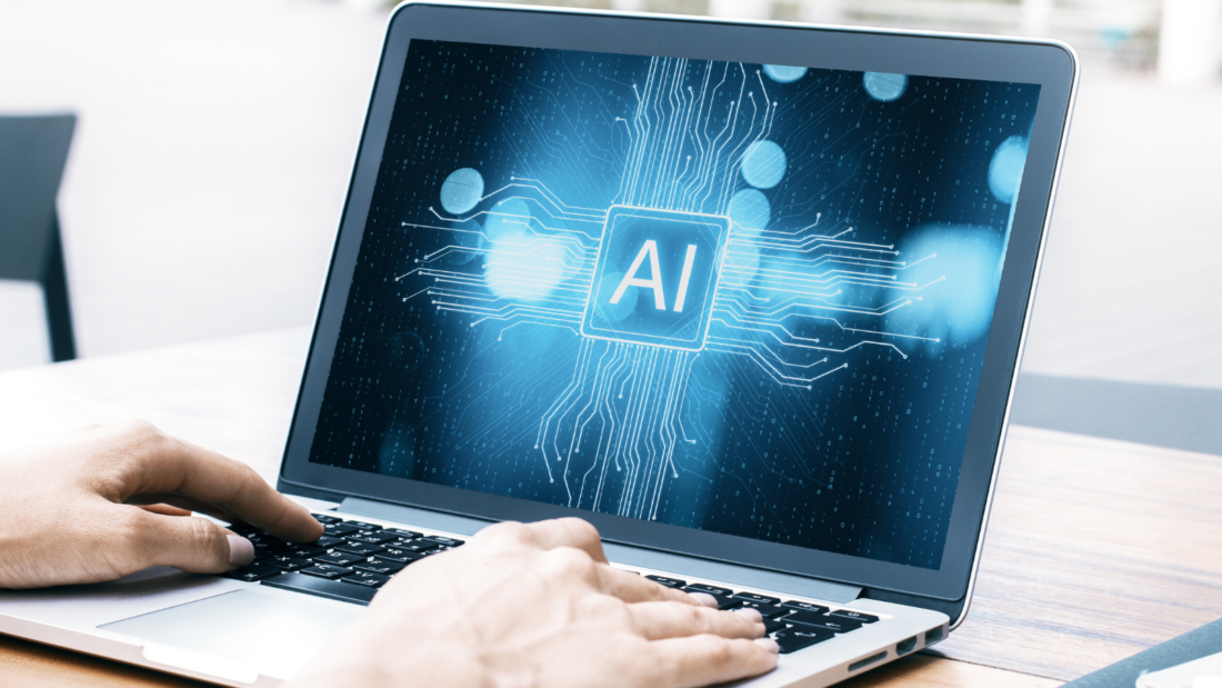 Zwei Hände am Laptop, auf dem Bildschirm steht "AI"