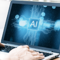 Zwei Hände am Laptop, auf dem Bildschirm steht "AI"