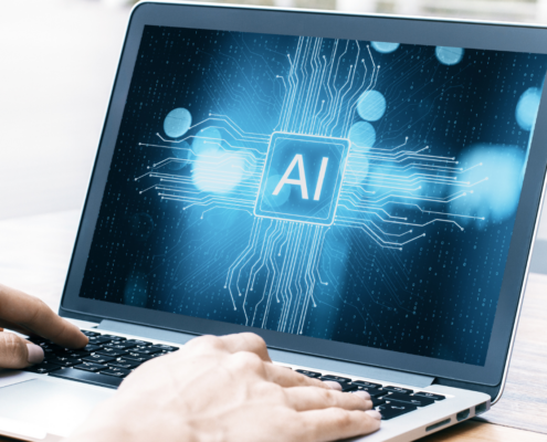 Zwei Hände am Laptop, auf dem Bildschirm steht "AI"