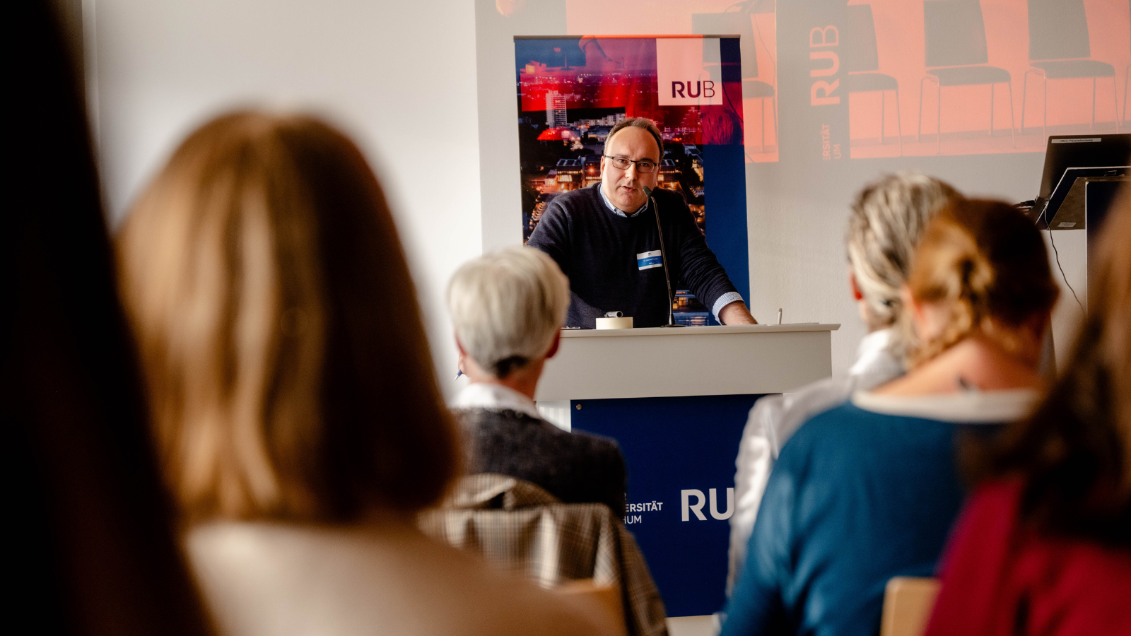 Joachim Preusse steht am Rednerpult und eröffnet die Tagung. Publikum im Vordergrund