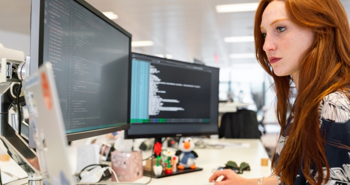 Frau mit rötlichen Haaren am PC, die Monitore zeigen Ordnerstrukturen an