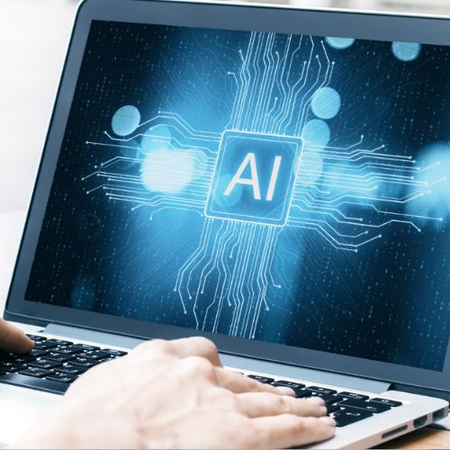 Zwei Hände am Laptop, auf dem Bildschirm steht "AI"