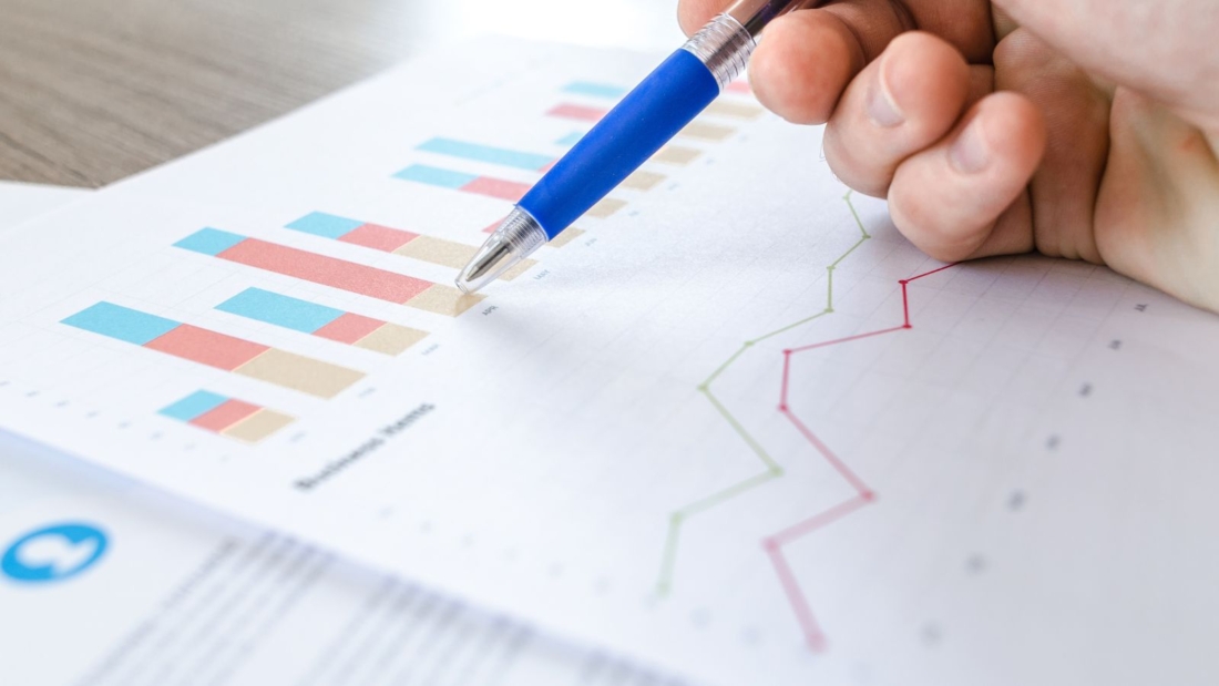 Diagramme auf einem Blatt Papier, darüber eine Hand mit blauem Kugelschreiber