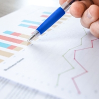 Diagramme auf einem Blatt Papier, darüber eine Hand mit blauem Kugelschreiber