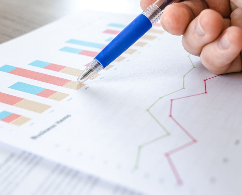 Diagramme auf einem Blatt Papier, darüber eine Hand mit blauem Kugelschreiber