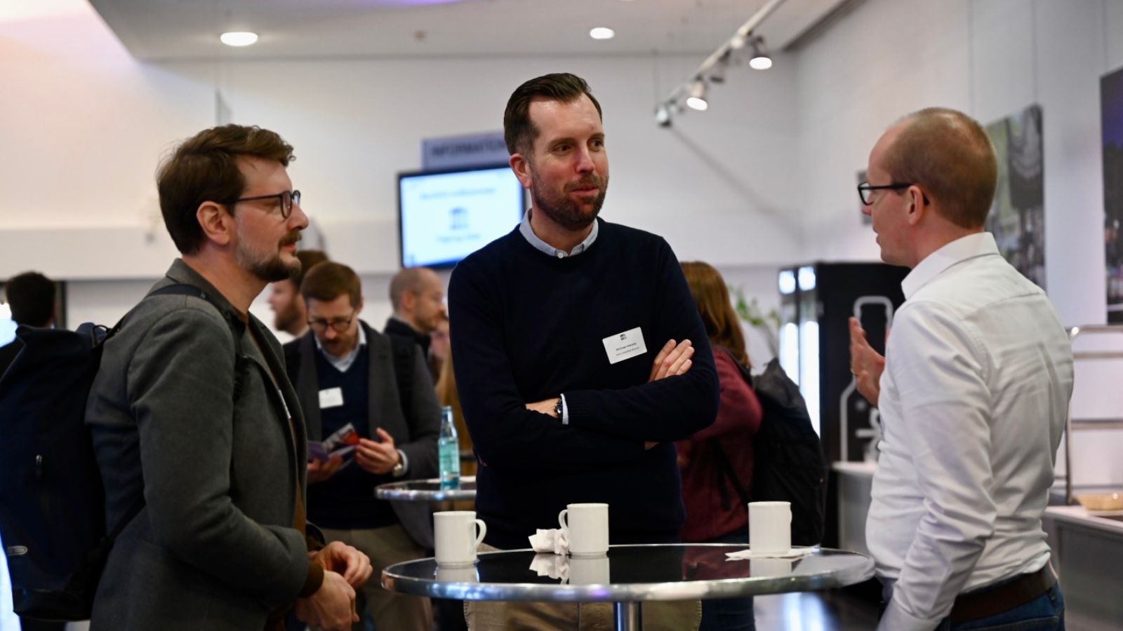 Drei Männer unterhalten sich an einem Stehtisch.