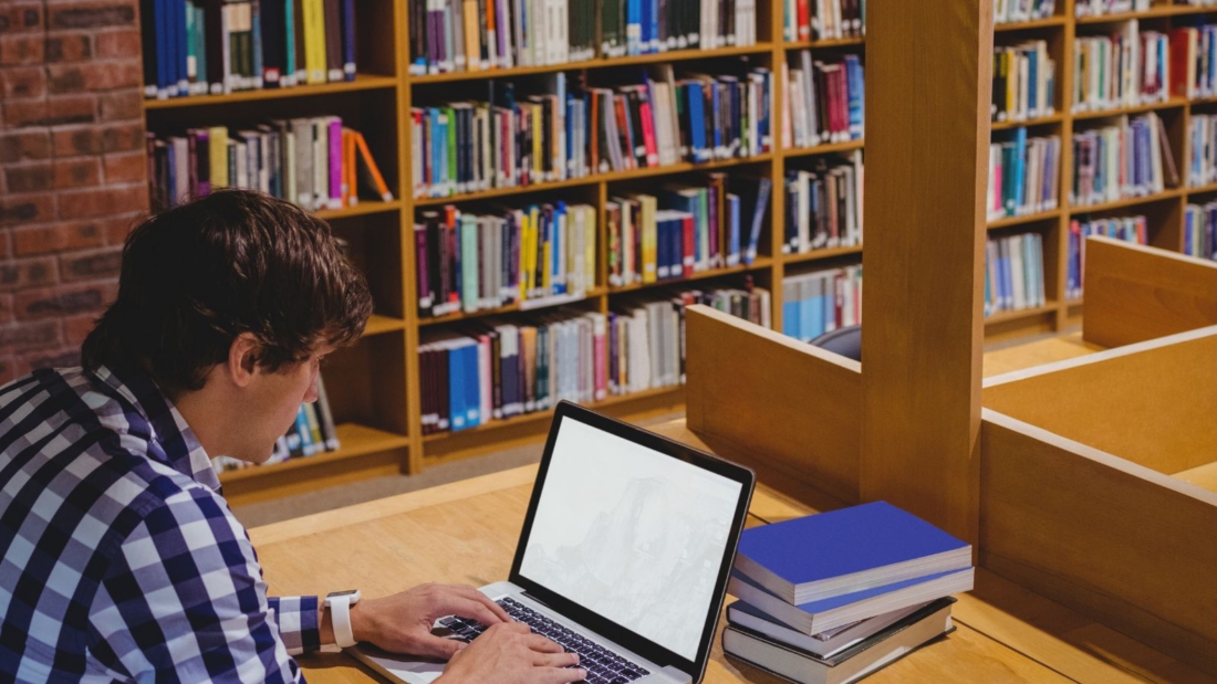 Mann sitzt in Bibliothek am Rechner.