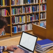 Mann sitzt in Bibliothek am Rechner.