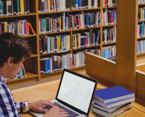 Mann sitzt in Bibliothek am Rechner.