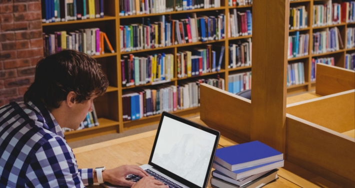 Mann sitzt in Bibliothek am Rechner.