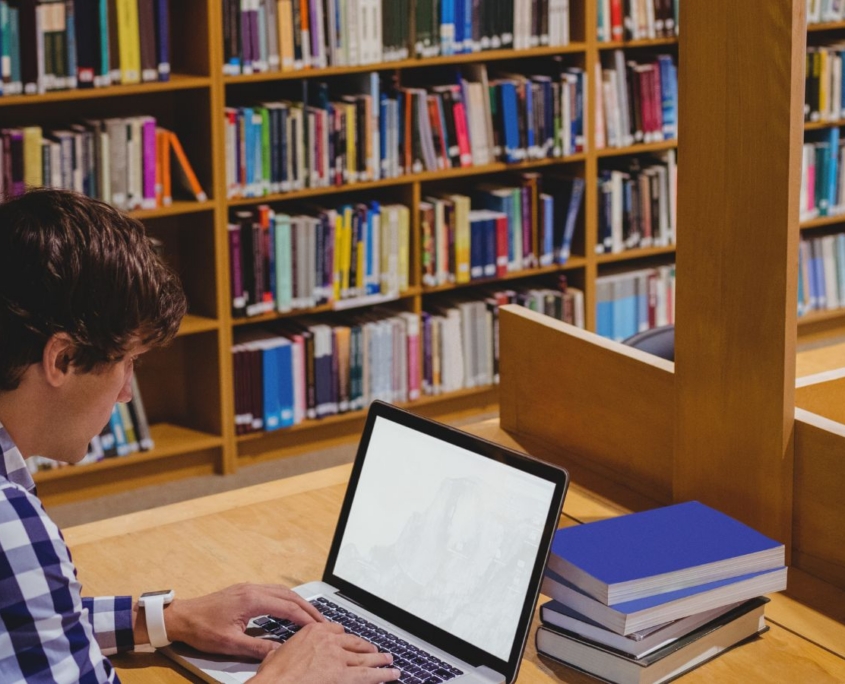 Mann sitzt in Bibliothek am Rechner.