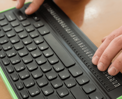 Zwei Hände tippen auf einer Computer-Braille-Tastatur.